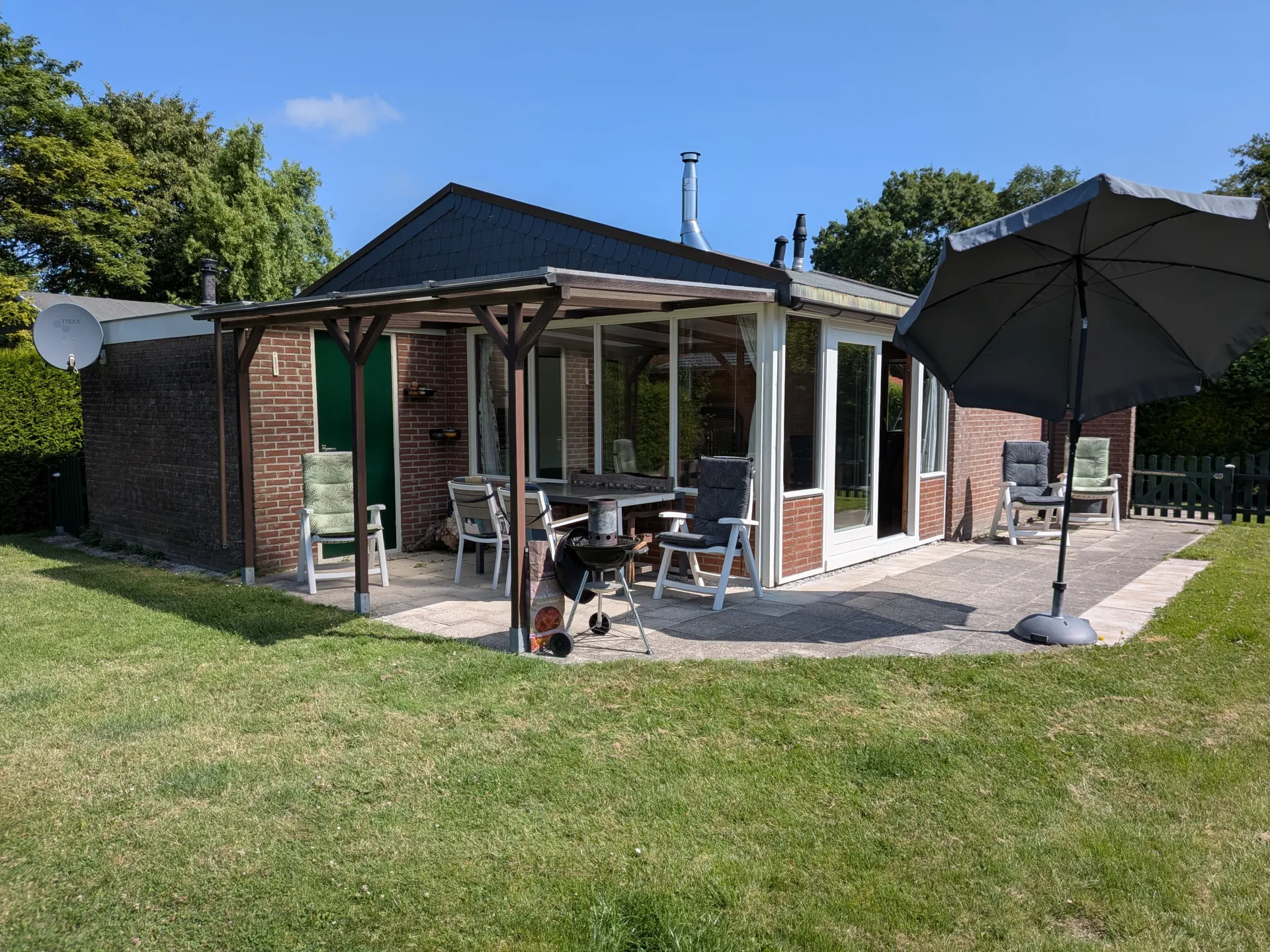 Patio with dining table, chairs and parasol behind the house